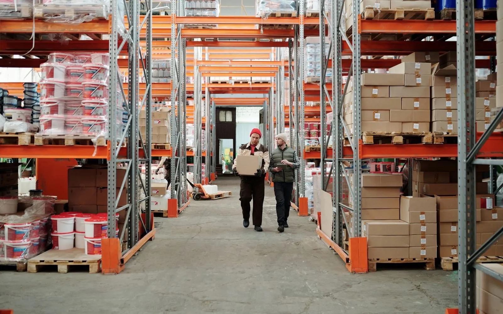 Hai nhân viên kiểm hàng giữa lối đi kho chứa đầy pallet